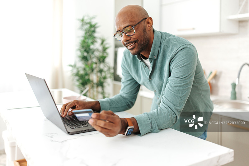 男人在厨房用笔记本电脑输入付款信息图片素材