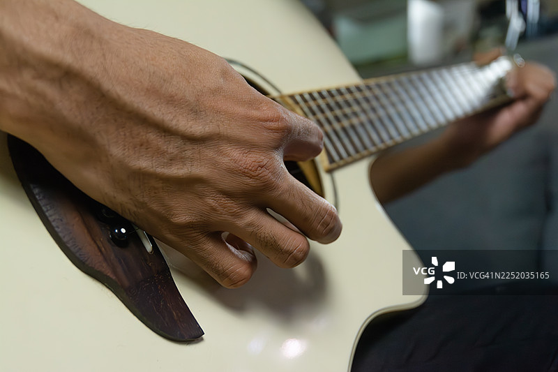 亚洲男子在舒适的客厅沙发上弹奏原声吉他图片素材