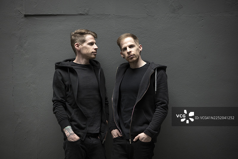 双胞胎兄弟站在深色墙壁前图片素材