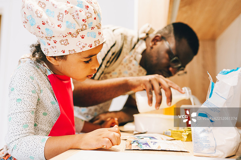 混血父亲和年幼的女儿在晨光中的厨房里制作面糊食材图片素材