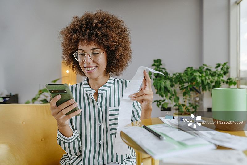 非裔女性在家中使用智能手机计算财务账单图片素材