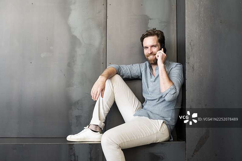 快乐的商人在办公室大厅边打电话边坐着图片素材