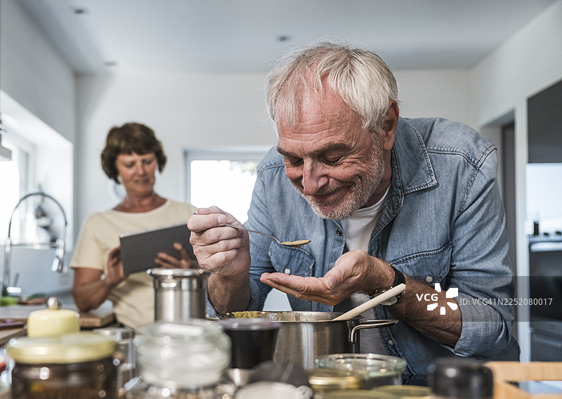 一位年长的男性在厨房里闭着眼睛品尝食物图片素材