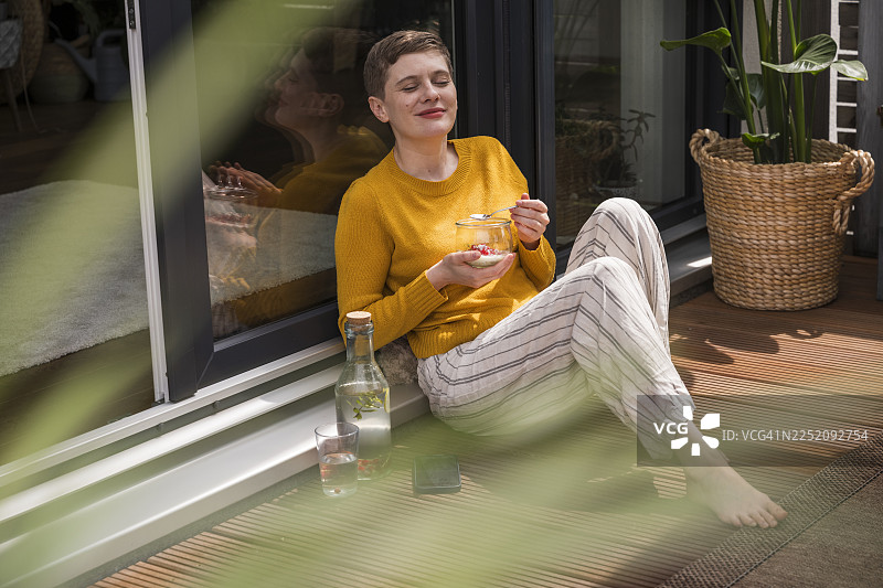 阳光下，一位女士在露台上享受着茶点和健康食品，脸上洋溢着笑容图片素材