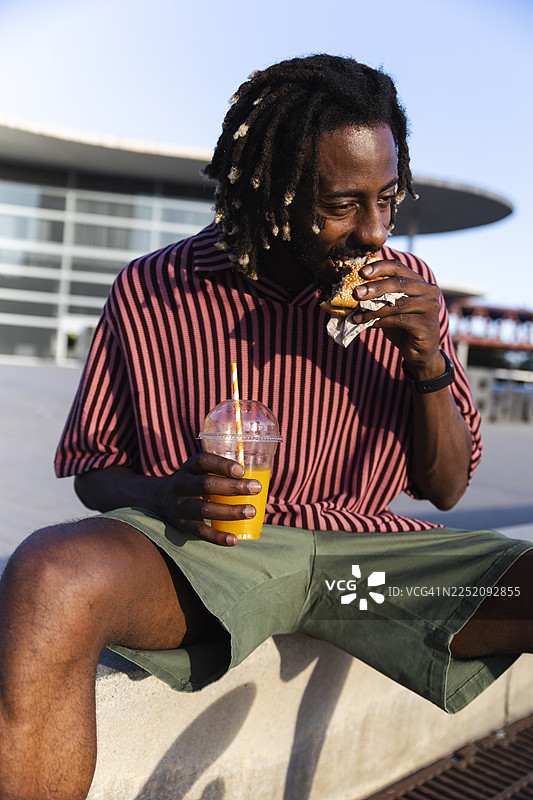 穿着休闲服的滑板运动员在户外吃汉堡喝果汁图片素材