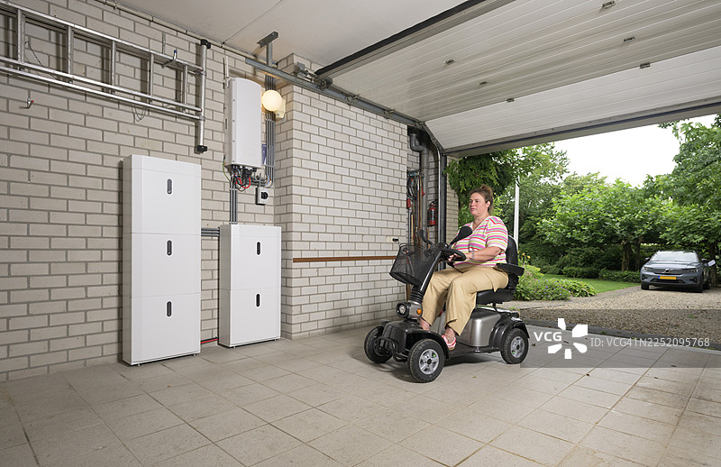 一个人在车库里使用电动滑板车，并配有用于储存多余电力的电池组图片素材
