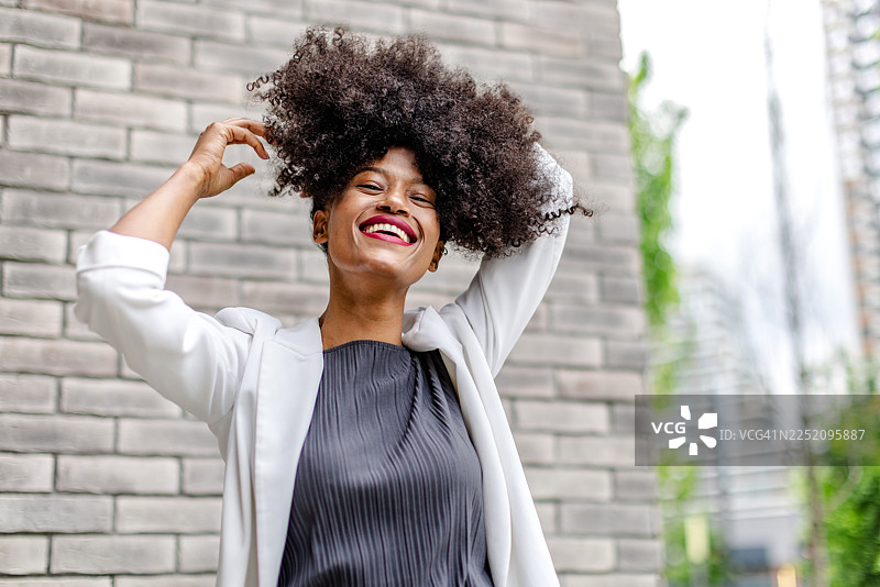 一个年轻的黑人女性，有着自然发型，在阳光明媚的城市户外，脸上洋溢着喜悦的表情。图片素材