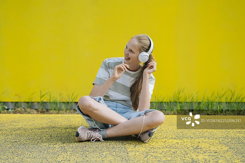 戴着耳机听音乐的女孩坐在黄色墙边图片素材