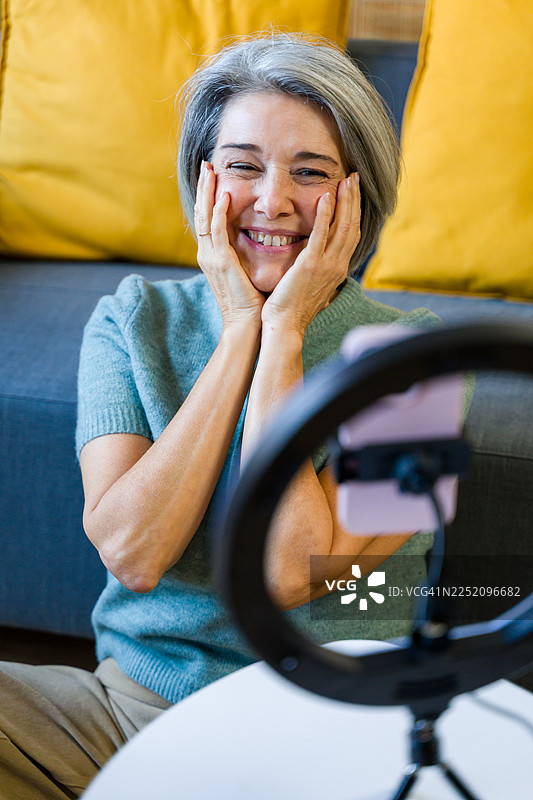 一位年长的女性在家中使用智能手机和环形灯进行视频博客录制图片素材