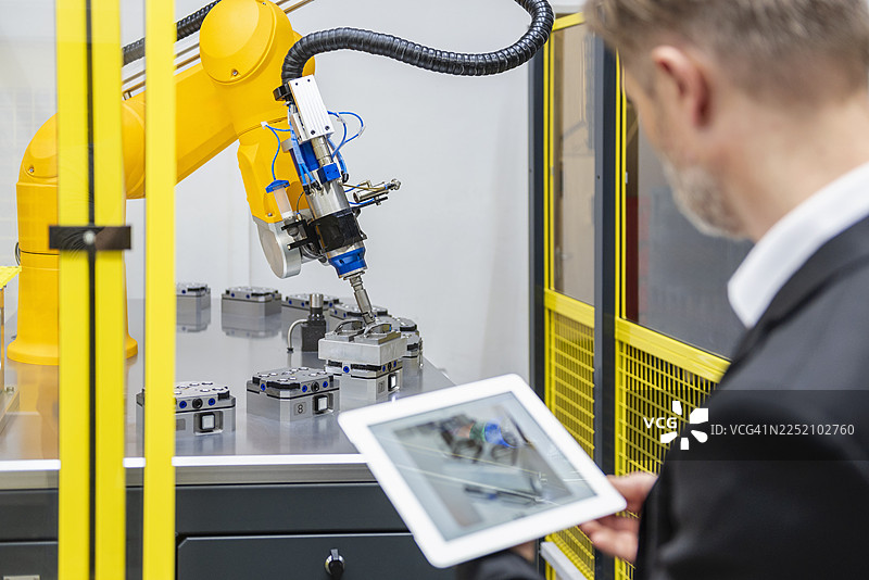 工程师在现代化的工厂中使用平板电脑监控工业机器人手臂图片素材