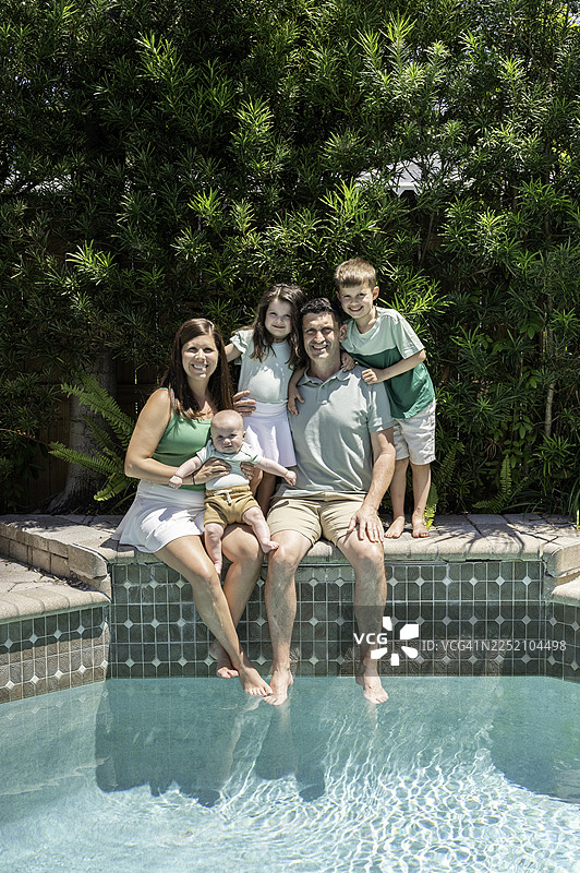 可爱的年轻家庭，父母和三个年幼的孩子，在泳池边拍摄休闲温馨的家庭肖像图片素材