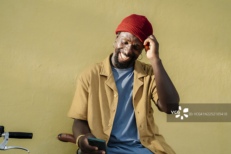 戴着红色绒线帽的男人微笑着看着智能手机，旁边停着一辆自行车图片素材