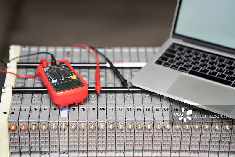 笔记本电脑和万用表正在测试电动汽车混合动力电池组图片素材