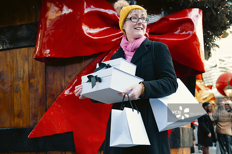 一位女士在节日的伦敦购物，手里拿着礼品盒和购物袋，脸上带着笑容图片素材