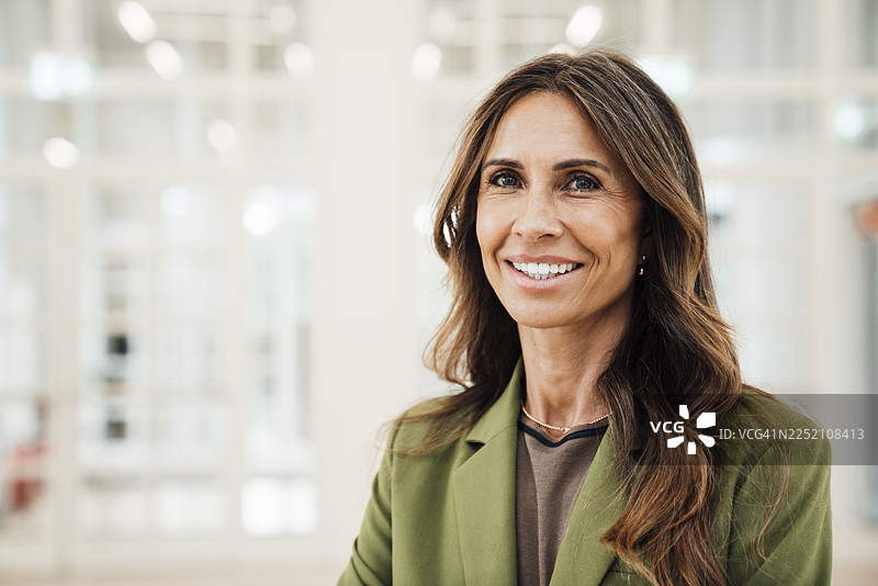 身穿绿色西装外套、面带微笑的商界女性在室内医疗诊所图片素材