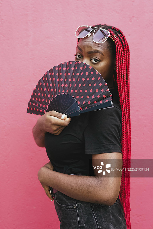 戴着太阳镜、留着红色脏辫的女人正拿着波点扇子图片素材