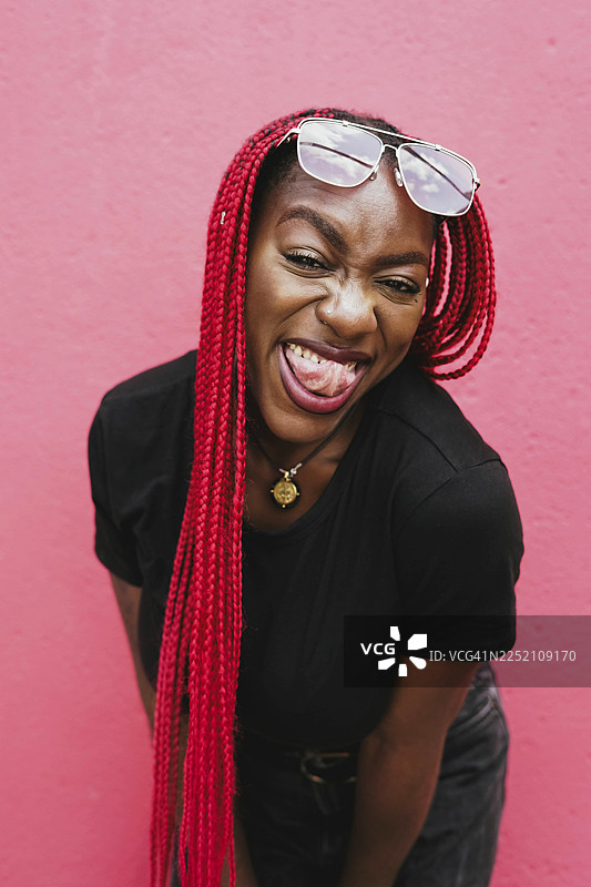 戴着太阳镜、梳着红色辫子的女士微笑着俏皮地摆姿势图片素材