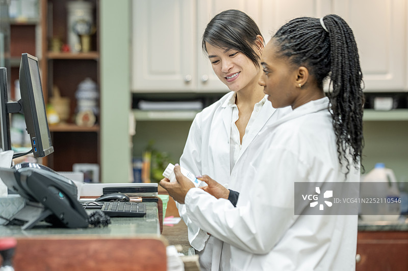 亚裔医生与非裔药剂师在实验室柜台前合作，手中拿着药瓶图片素材