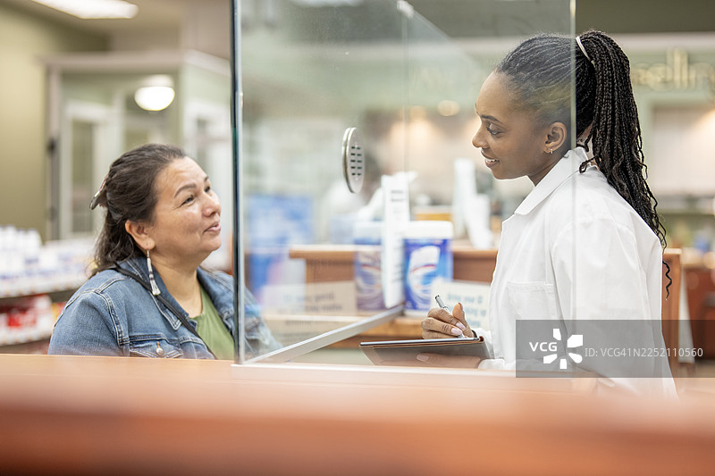 一位友善的黑人女药剂师在药房柜台协助一位西班牙裔顾客图片素材