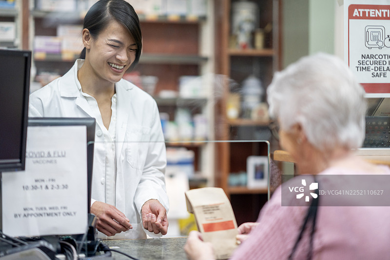 亚洲药剂师在药房柜台为老年妇女提供友好的客户服务图片素材