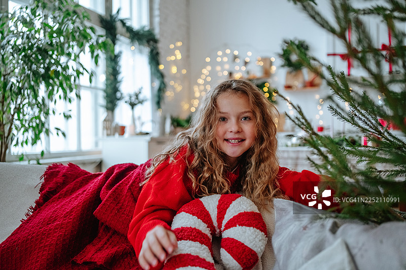 面带微笑的孩子在节日装饰的家中，舒适地躺在圣诞沙发上图片素材