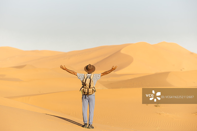 日出时，一个人在撒哈拉沙漠张开双臂徒步图片素材