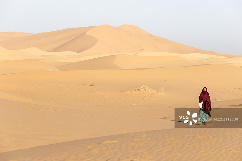 一个人站在撒哈拉沙漠中，周围是金色的沙子和广阔的空间图片素材