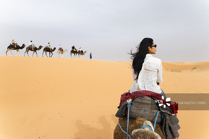 摩洛哥撒哈拉沙漠沙丘中骑着骆驼的旅行者图片素材