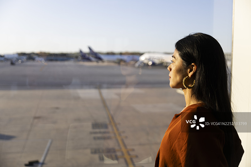 商务女性在机场航站楼的窗边，一边打电话一边拿着笔记本电脑图片素材