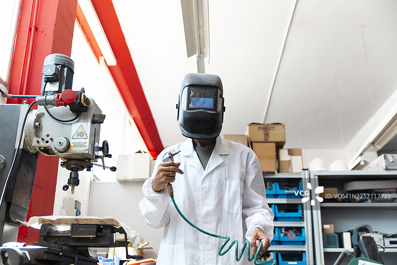 电子车间里，一位实验室技术人员戴着焊接面罩使用气焊枪。图片素材