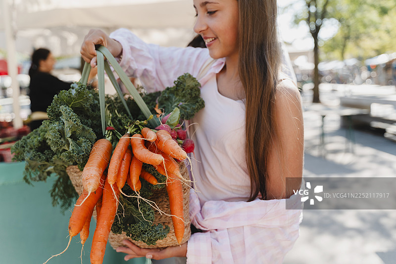 一位面带微笑的女孩在当地露天市场购买有机蔬菜图片素材