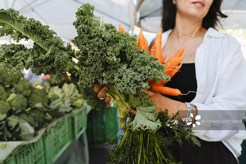 在本地市场，一个人拿着羽衣甘蓝和胡萝卜，倡导有机选择。图片素材