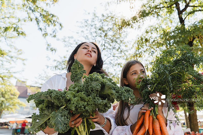 一位女士和她的女儿在本地市场手持有机羽衣甘蓝和胡萝卜图片素材