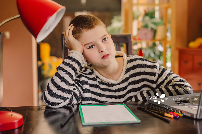 疲惫的男孩坐在室内桌前，用笔记本电脑做作业图片素材