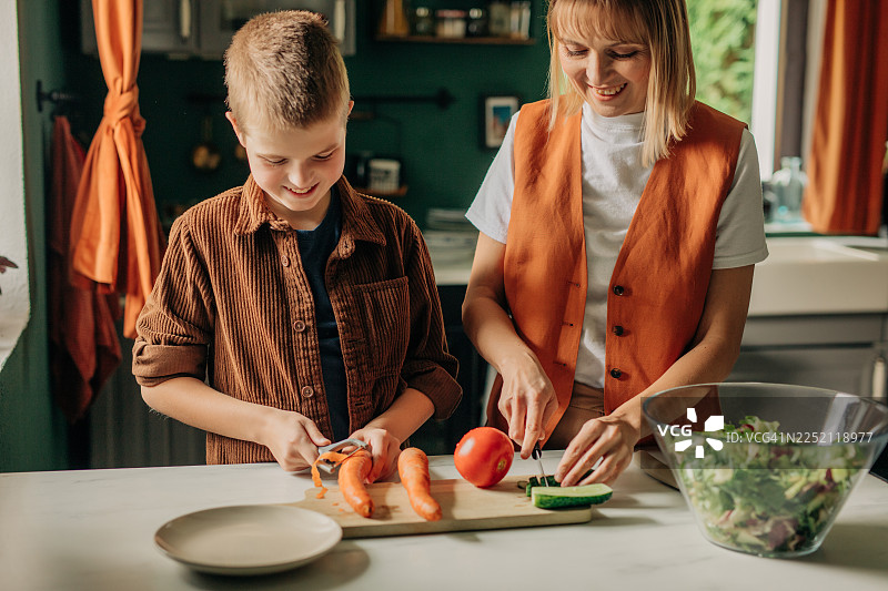 微笑的母亲和孩子在厨房里准备健康的蔬菜沙拉图片素材