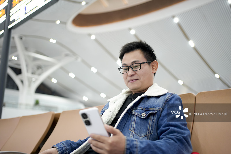 一位男士坐在候机厅，在等待登机时浏览手机图片素材