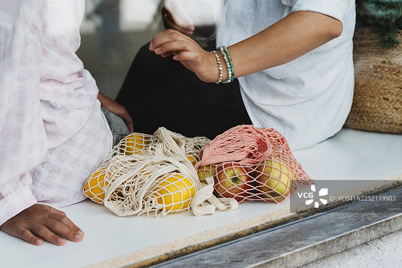 母亲和女儿用可重复使用的购物袋装满新鲜水果，享受亲子时光图片素材