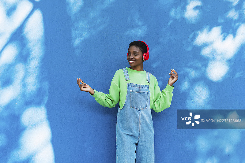 戴着无线耳机、在蓝色墙壁前快乐跳舞的年轻女子图片素材