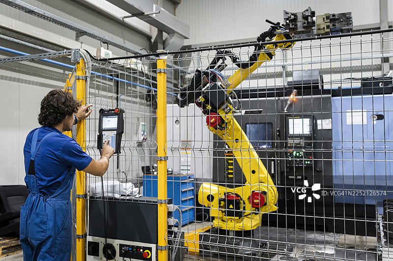 技术人员在工业环境中操作带有机械的机器人手臂图片素材