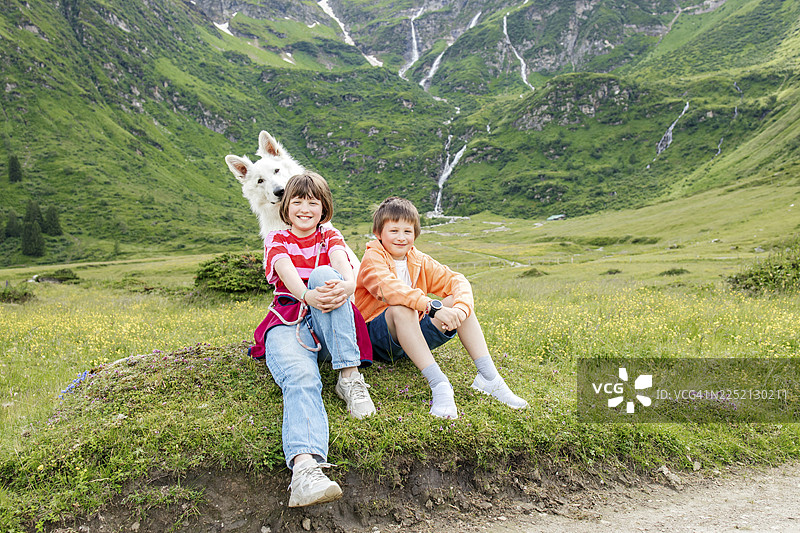 快乐的兄妹俩和一只狗坐在草地上图片素材