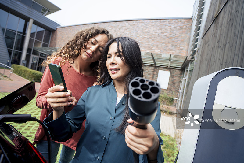 一位女士在充电站拿着电源插头，将智能手机分享给朋友图片素材