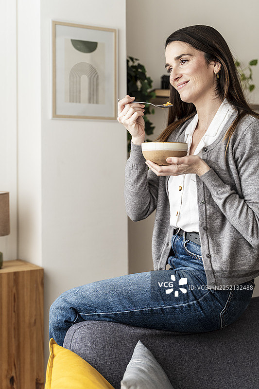 一个女人坐在沙发上，在舒适的室内环境中吃着碗里的食物图片素材
