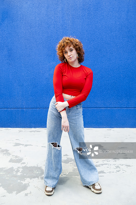 身着都市服饰的纹身女性自信地摆出姿势，背景为蓝色图片素材