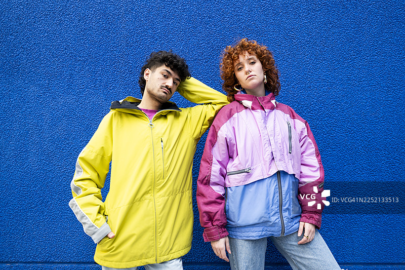 两个朋友穿着色彩鲜艳的城市服装，在蓝色背景前摆姿势图片素材