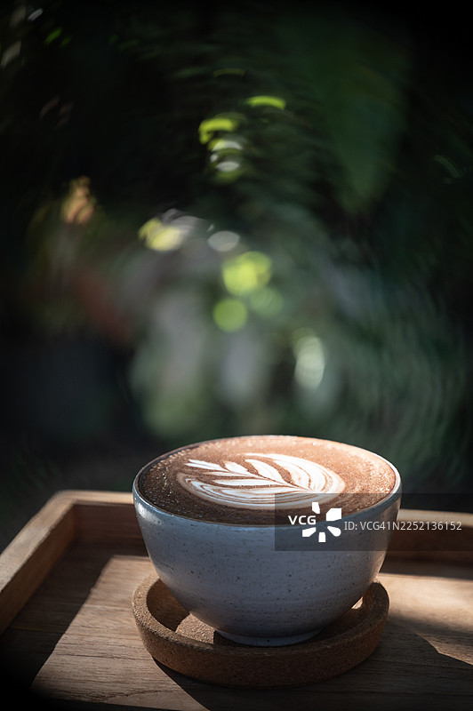花园里放着一个带有花卉图案的热巧克力杯，背景柔和模糊。图片素材