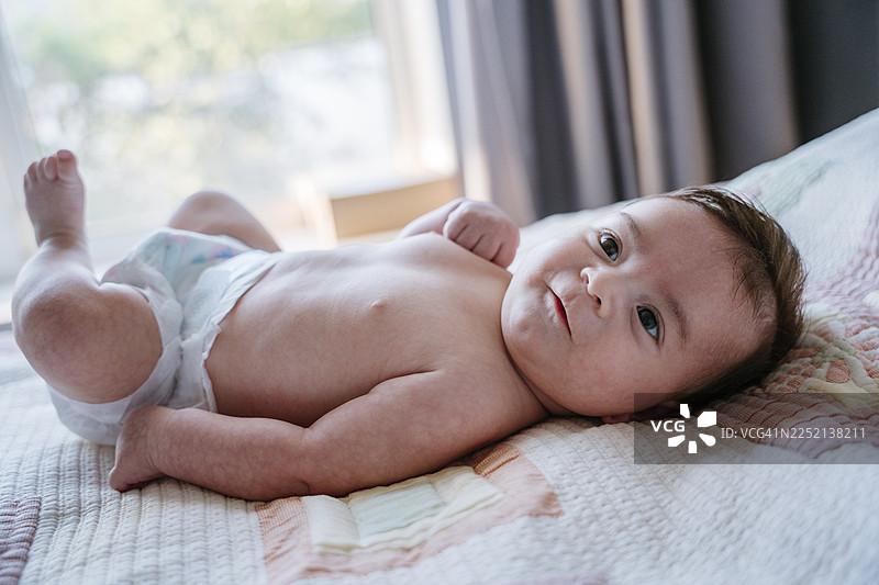 柔和的晨光中，婴儿舒适地躺在室内的床上。图片素材