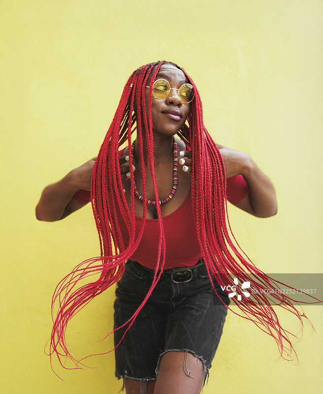 时尚女子留着红色长辫，在黄色墙壁前摆姿势图片素材