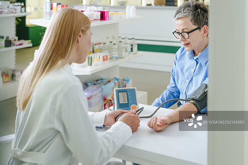 药剂师在药房咨询中为患者测量血压图片素材
