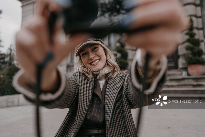 身穿格子外套和帽子，戴着帽子的女士在户外的石阶上微笑着自拍，定格秋日时尚瞬间图片素材