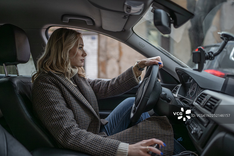 一位身穿格子外套、表情专注的女商人正驾驶着一辆现代轿车图片素材